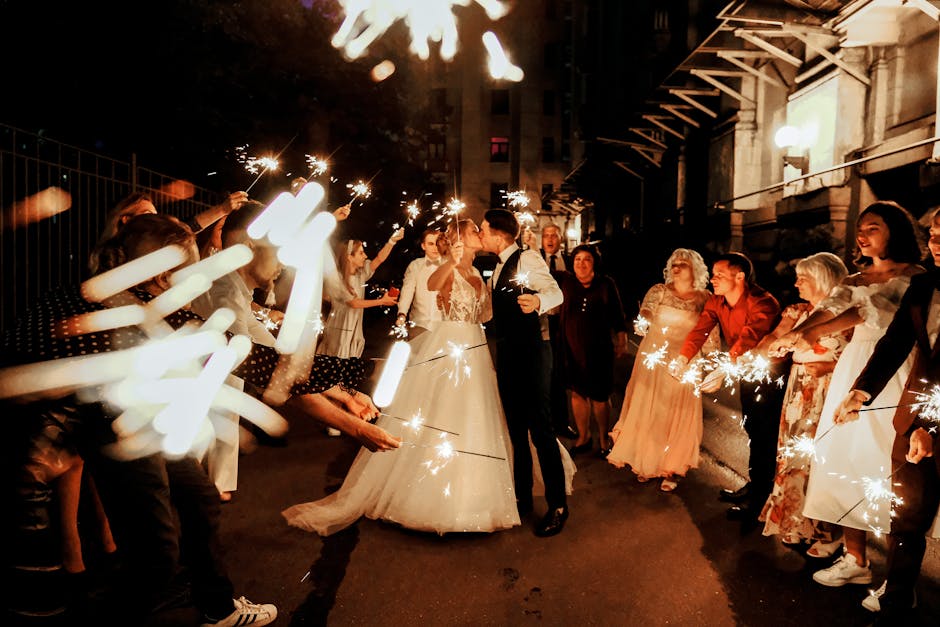 A newlywed couple surrounded by friends holding sparklers during an outdoor nighttime wedding celebration.