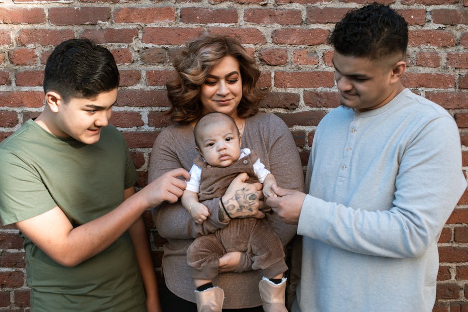 A joyful family holding a baby outdoors against a brick wall, highlighting love and unity.