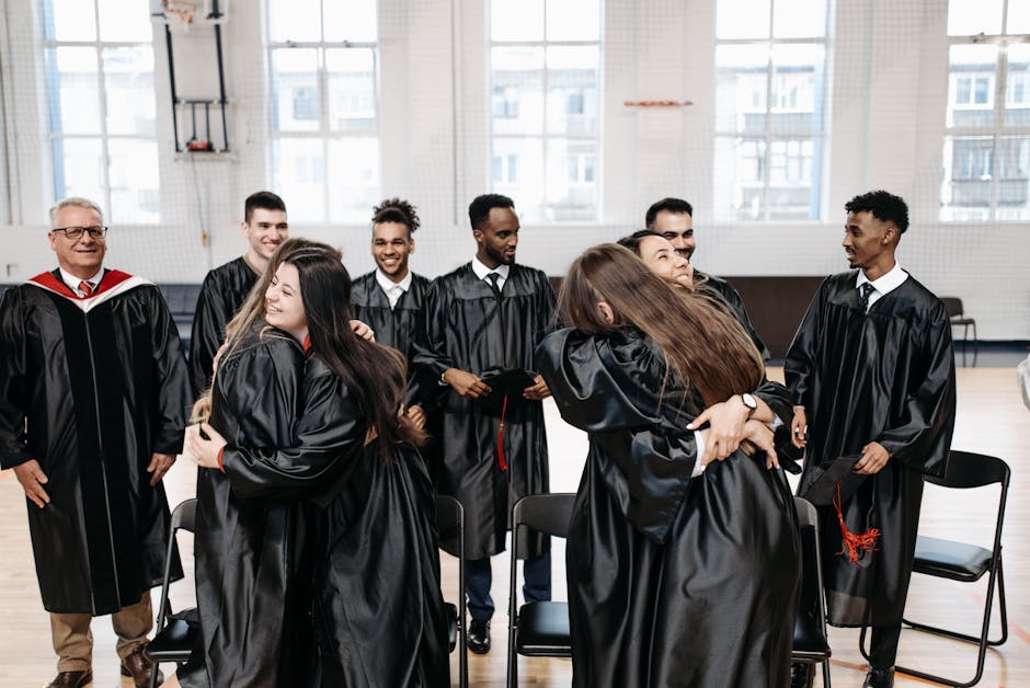 A joyful group of graduates hugging and celebrating their success in a gymnasium.
