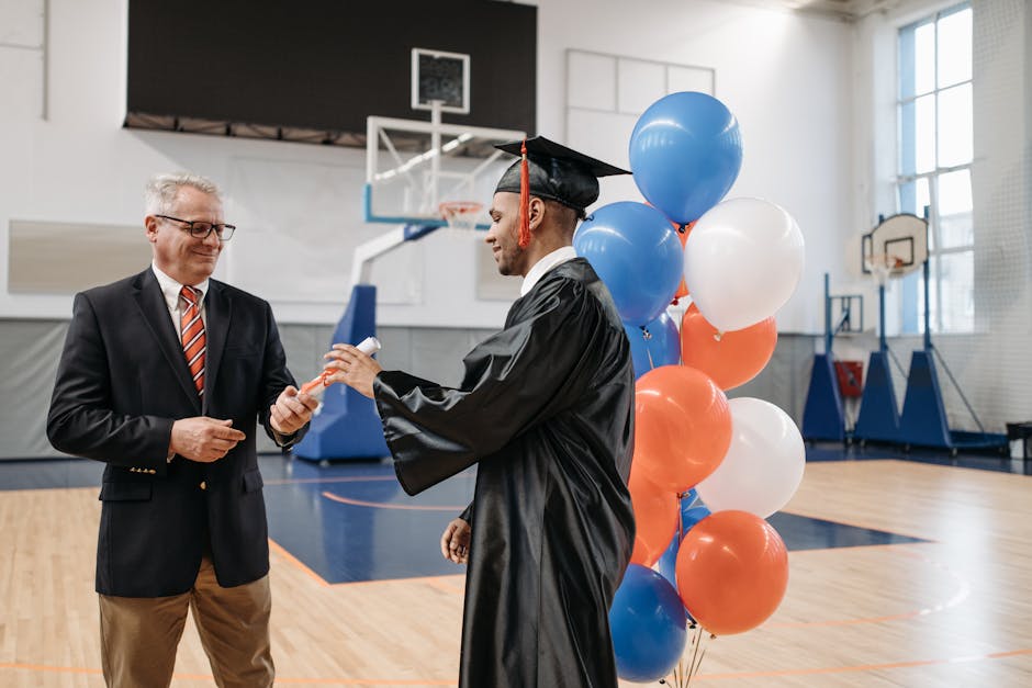 A joyful graduate receives a diploma from a school director during a ceremony in a gymnasium.
