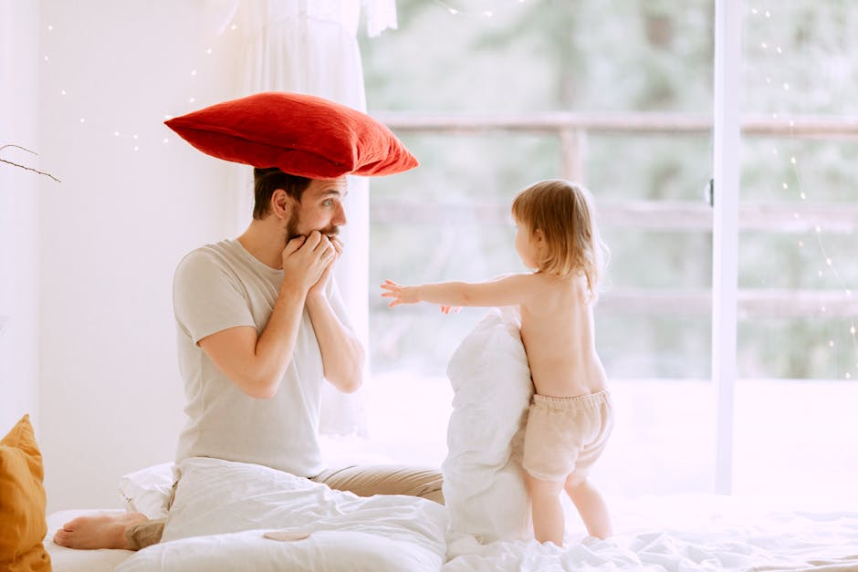 A joyful father and toddler are playfully engaging in a pillow fight at home.