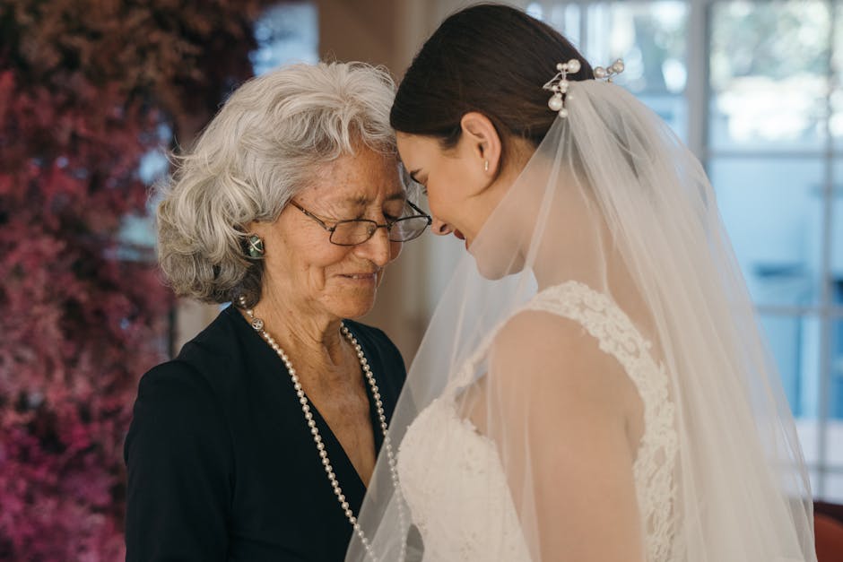 A bride shares an emotional connection with an elderly woman, eyes closed in a heartfelt moment.