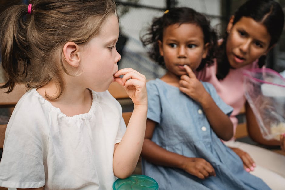 Three diverse girls enjoy snacks together, sharing a joyful moment on an outdoor bench.