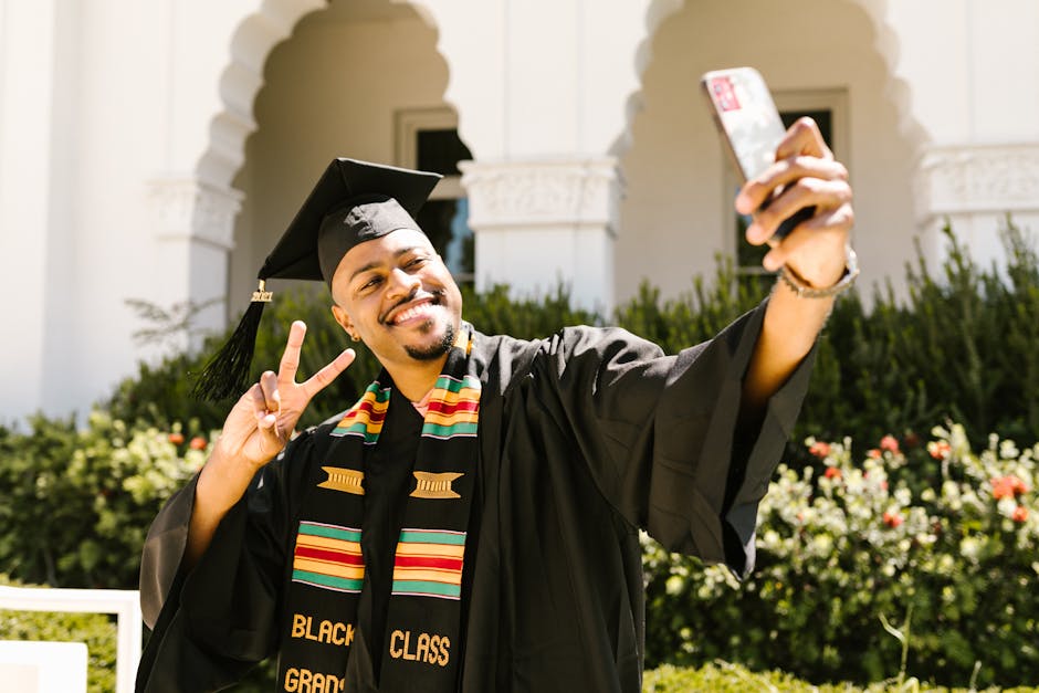 Joyful graduate in cap and gown taking a selfie outdoors for celebration.