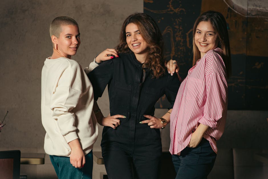 Three friends smile and pose in a casual indoor setting, showcasing diverse styles.