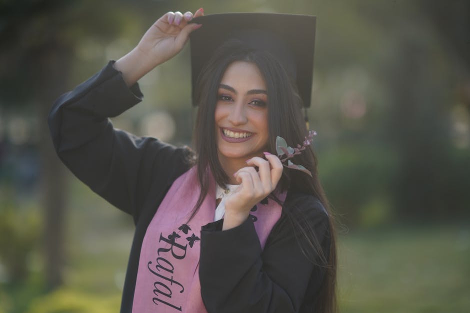 Young graduate woman smiling in cap and gown, celebrating her success outdoors.