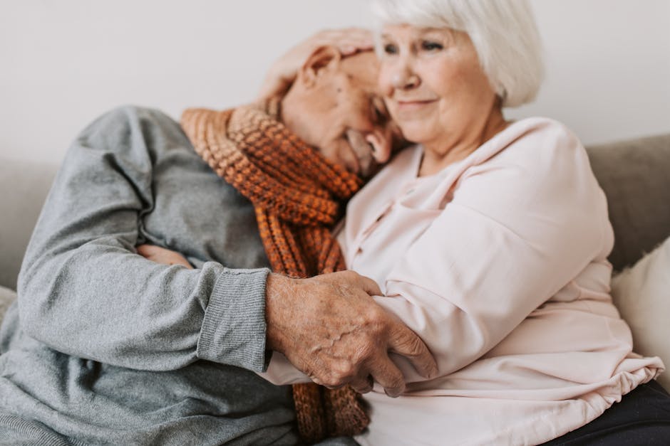 An elderly couple sharing a loving embrace while sitting on a cozy couch.