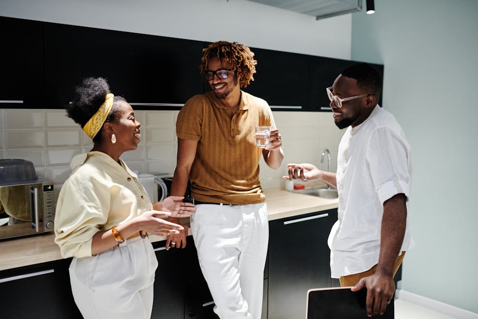 A joyful group of colleagues in an office kitchen, laughing and conversing during a break.