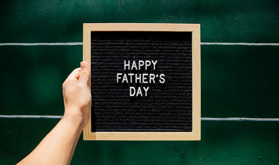 A person holding a 'Happy Father's Day' sign against a green wall, ideal for holiday greetings.