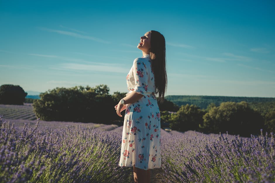 A woman in a floral dress enjoys the lavender field on a sunny day.