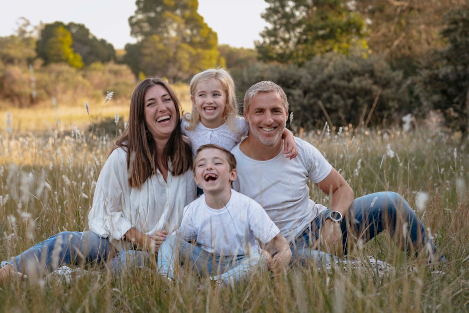 Smiling family of four sitting happily in a grassy field during fall.