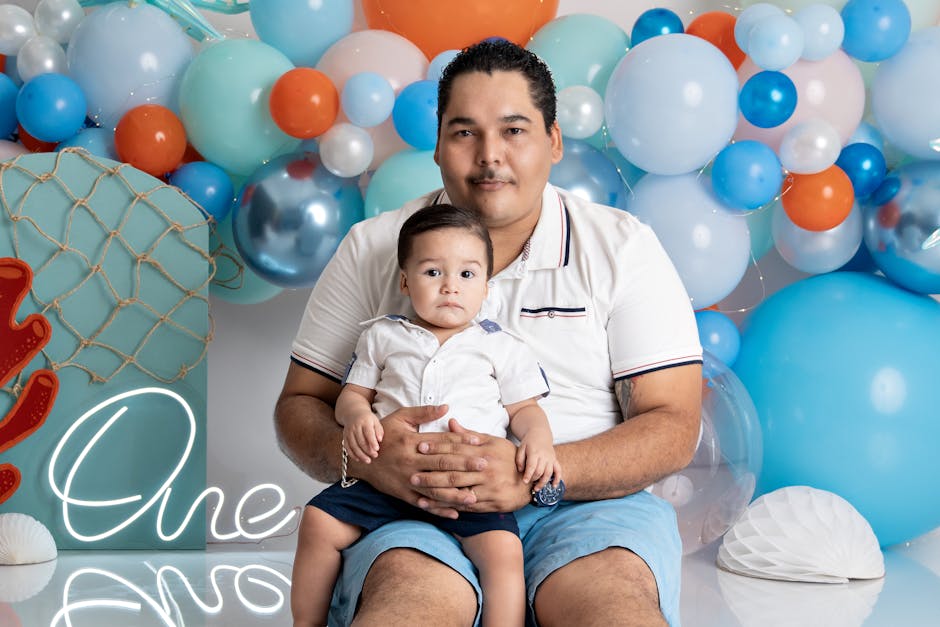 Father holding son at vibrant one-year birthday party with colorful balloons.