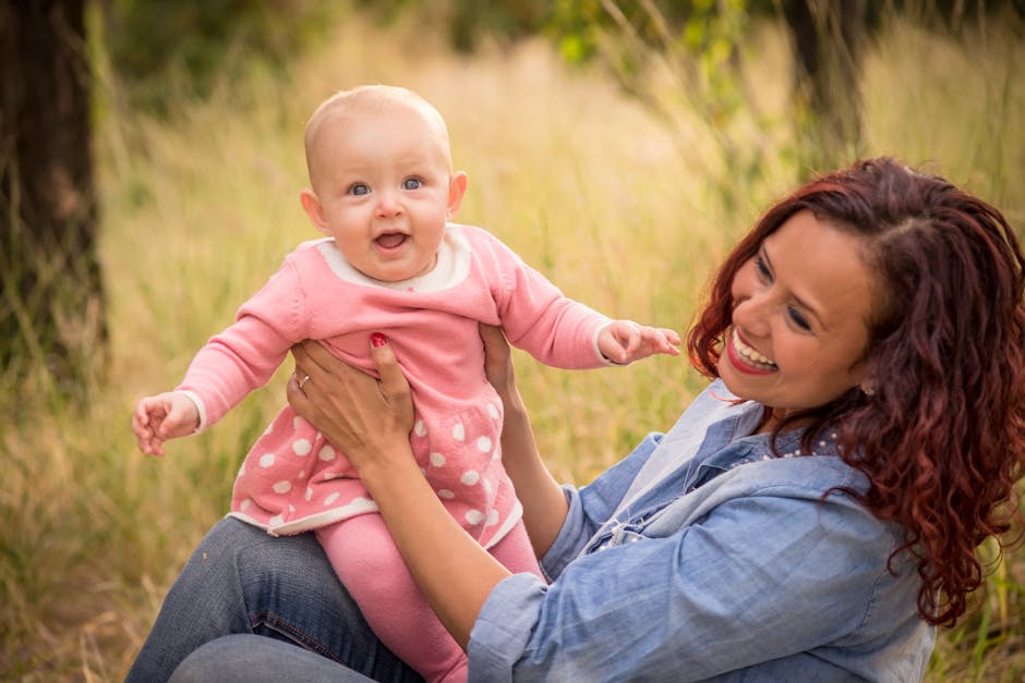 Joyful mother and baby girl smiling together outdoors in a sunny nature setting.