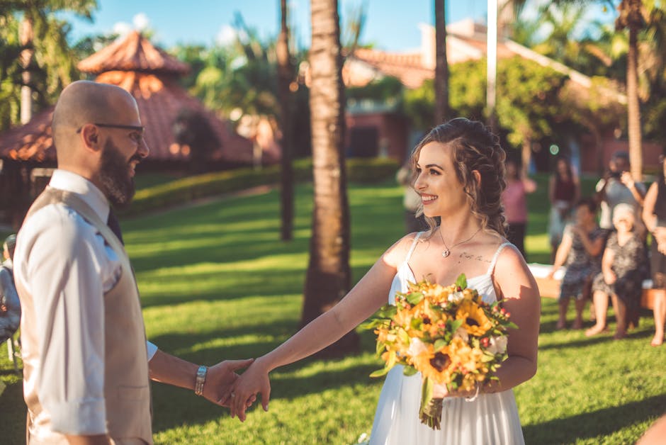 A joyful bride and groom hold hands during a sunny outdoor wedding ceremony surrounded by lush greenery.