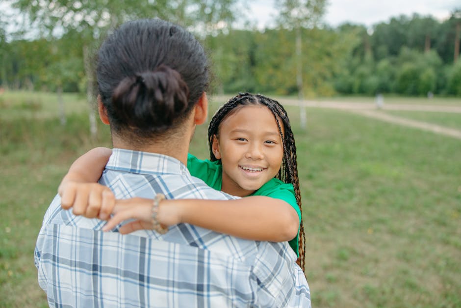 A joyful child with braided hair embraces a parent in a park setting, embodying love and happiness.