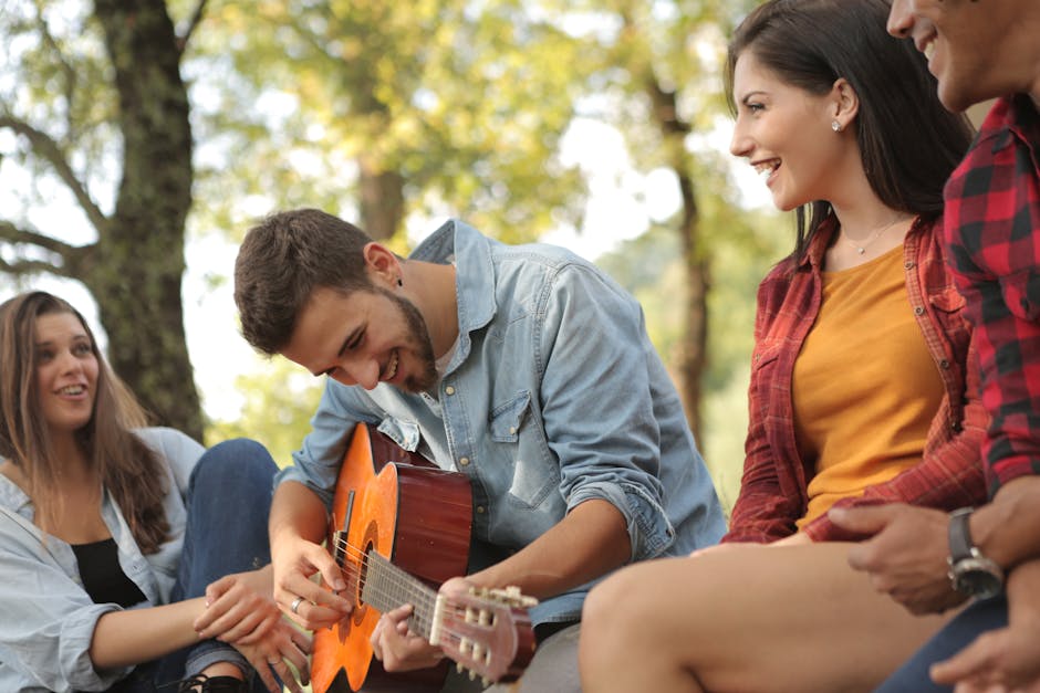 Young friends having fun playing guitar and laughing outdoors in a sunny park.
