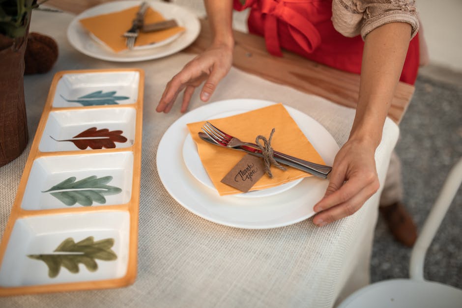 A person sets a Thanksgiving table with autumn-themed plates and a 'thank you' card.