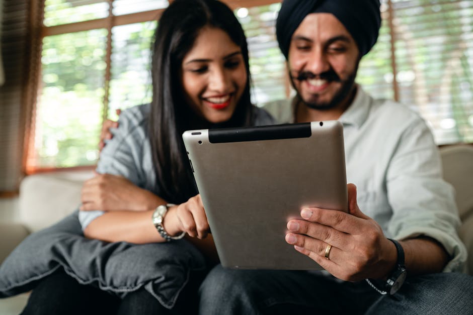 A cheerful couple enjoying leisure time using a tablet indoors, smiling and bonding.