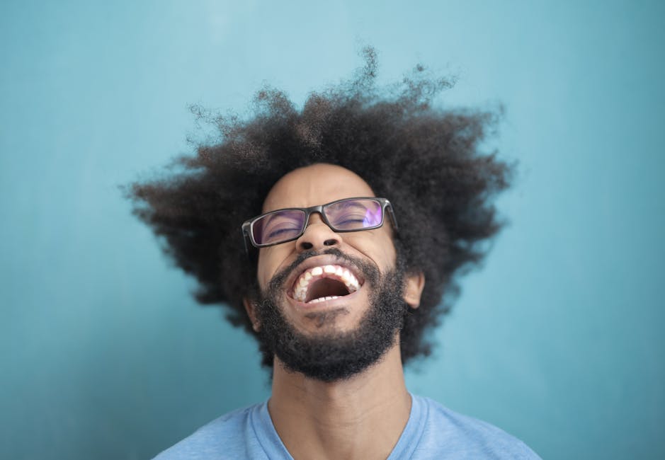 Close-up of a happy man with glasses and wild hair laughing against a blue background.