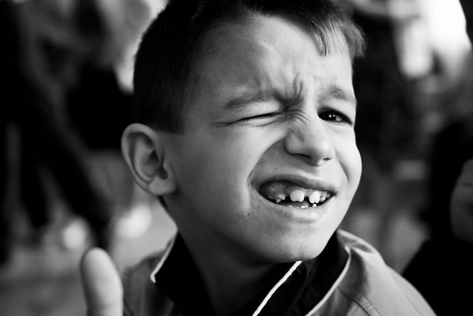 A playful young boy winking with a wide smile captured in a black and white close-up.