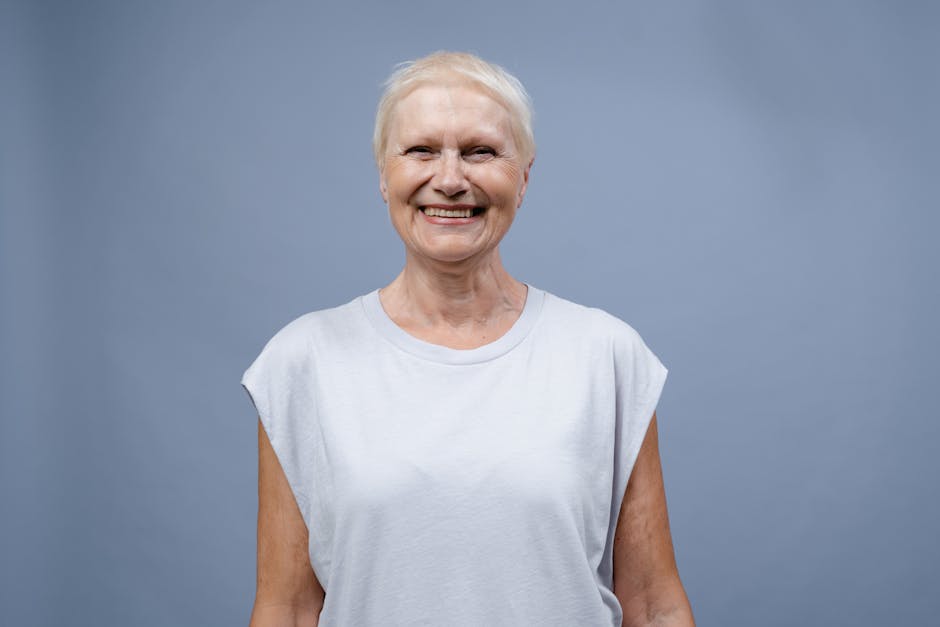 A joyful senior woman smiling warmly in a simple portrait against a blue backdrop.