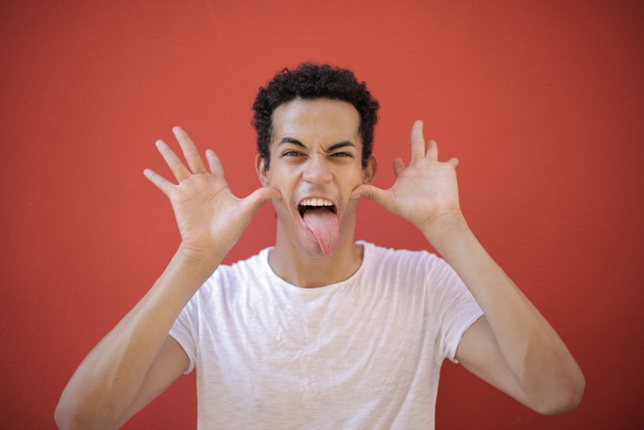 A cheerful young man making a funny face with his tongue out against a red background.