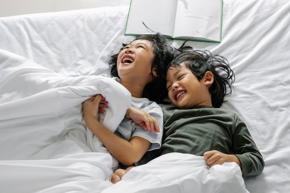 Happy siblings enjoying a playful moment in bed, surrounded by cozy blankets and laughter.