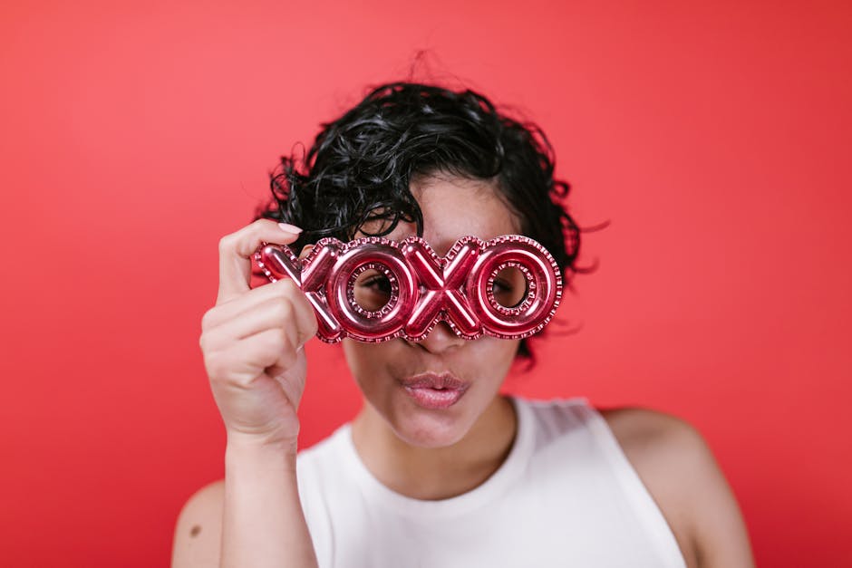 Woman posing with XOXO glasses against a red backdrop, perfect for Valentine's themes.