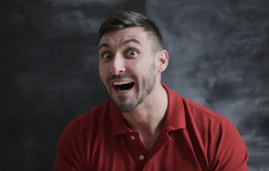 Close-up portrait of a man with a surprised expression wearing a red shirt.