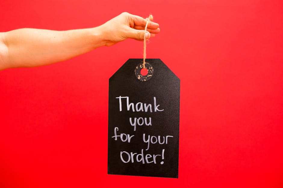 A hand holding a thank you sign for orders against a bold red background.