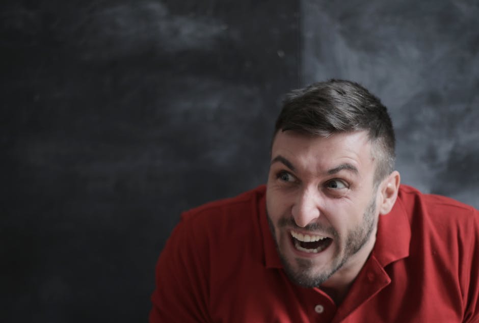 Portrait of a joyful man in a red polo shirt with a dynamic expression against a dark background.
