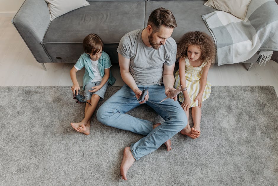 Father and children playing with toys on a gray carpet in a cozy living room from above.