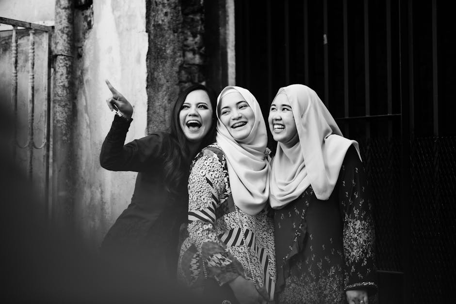 Three women in hijabs share a joyful moment and laughter during an outdoor photoshoot.