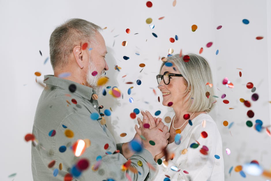 Happy senior couple smiling and celebrating with colorful confetti indoors.