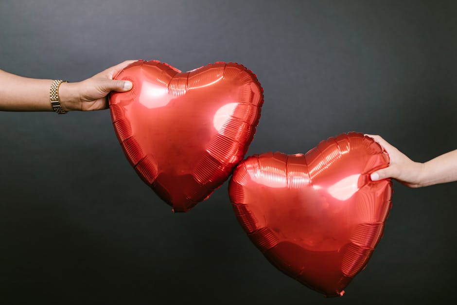 Two hands holding heart-shaped balloons against a black background, symbolizing love and romance.
