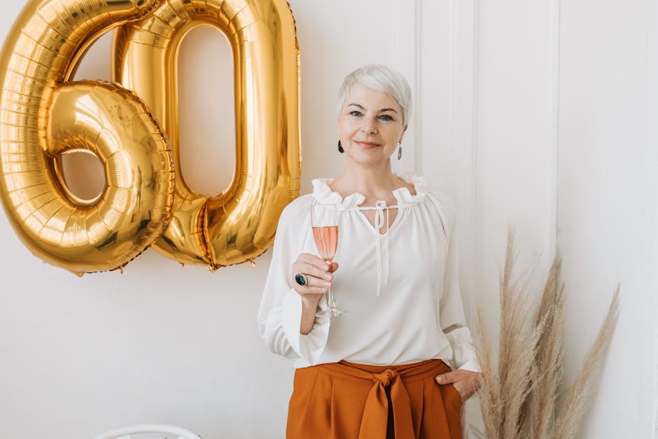 Senior woman joyfully celebrating her 60th birthday with a champagne toast and gold balloons.