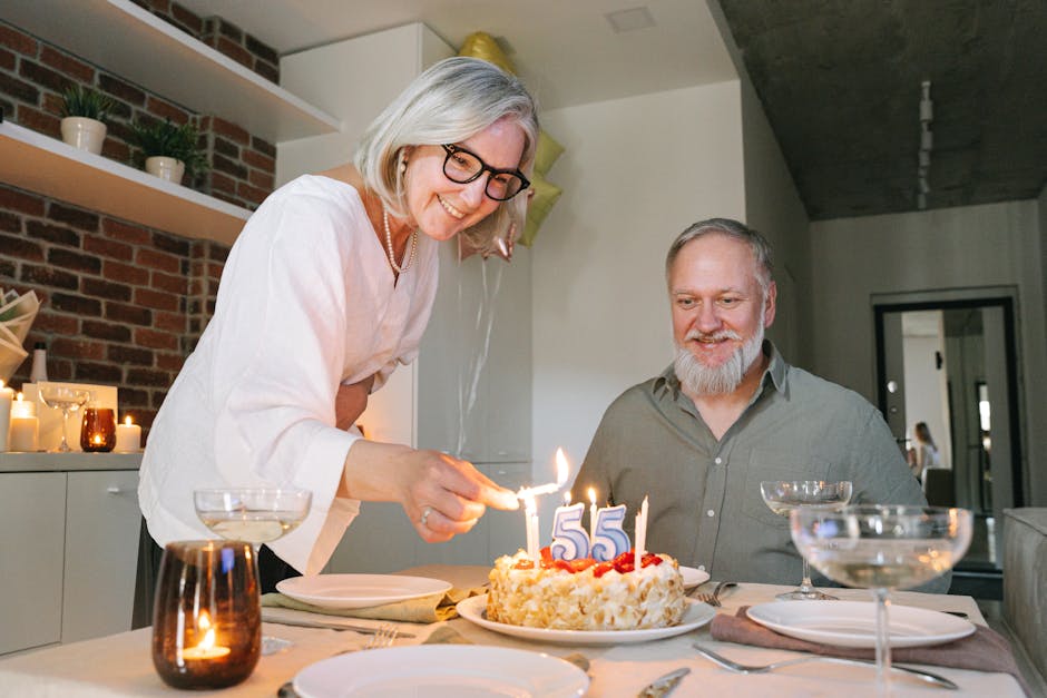 A joyful senior couple celebrates a 55th birthday with a cake at home, surrounded by warm candles.