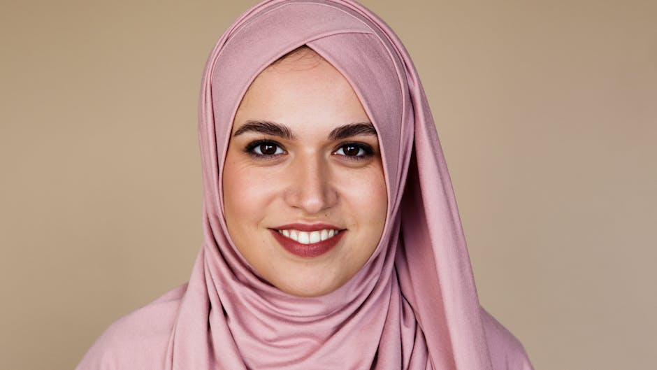 Portrait of a smiling woman wearing a pink hijab against a neutral background.
