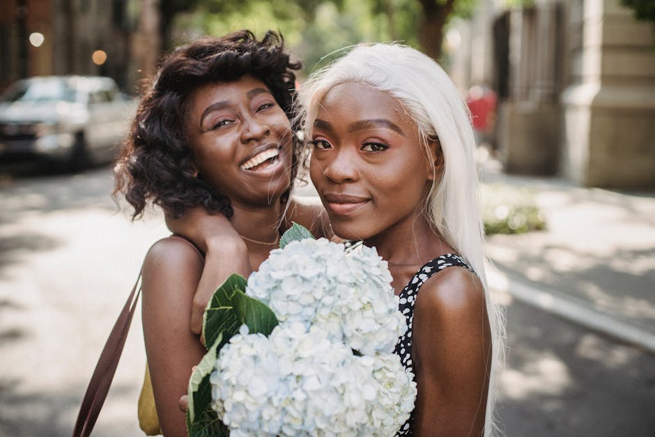 Two friends embrace outdoors with a bouquet of white flowers, radiating happiness.