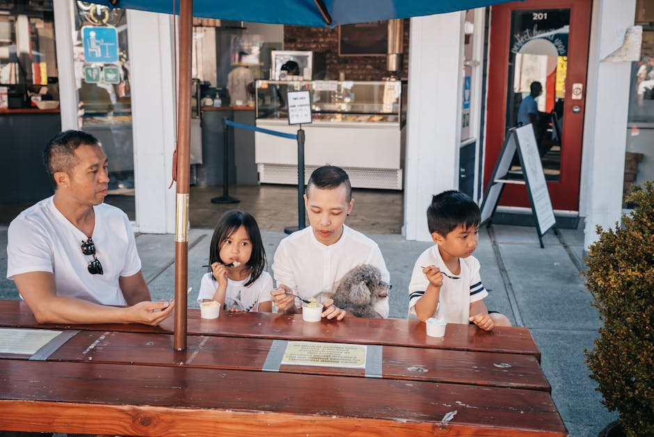A family of four shares ice cream together at an outdoor seating near an ice cream shop.