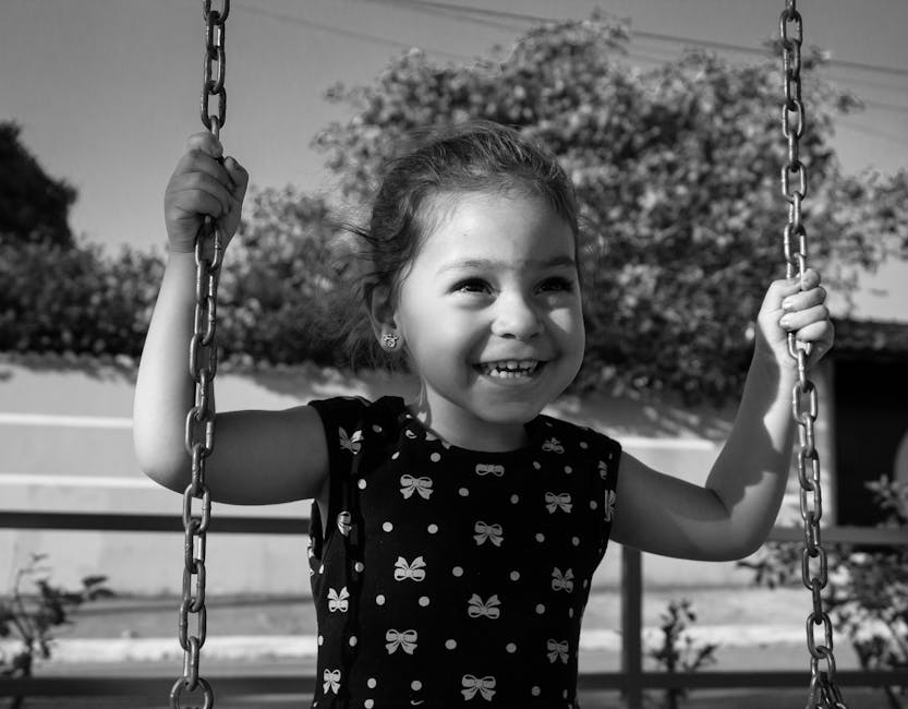 Smiling young girl having fun on a swing in a black and white outdoor setting.