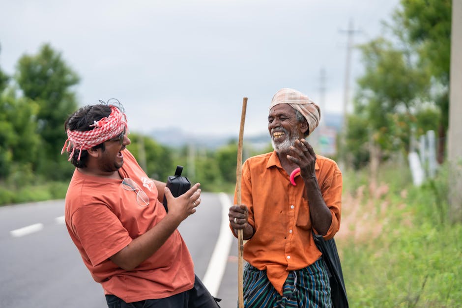 Smiling man sharing a laugh with an older gentleman on a rural roadside, capturing a heartwarming interaction.