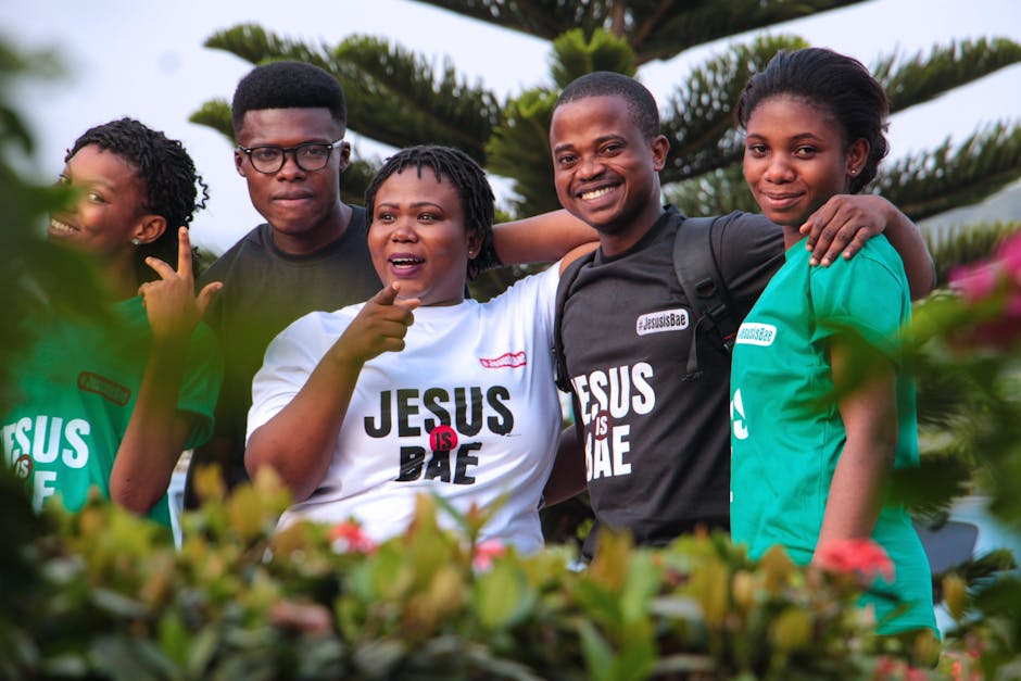 A cheerful group of friends posing in 'Jesus is Bae' shirts amidst greenery.