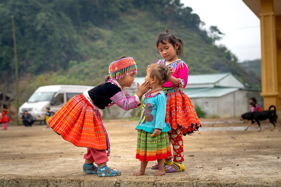 Three Asian children bond in colorful traditional dresses outdoors, reflecting cultural joy and friendship.