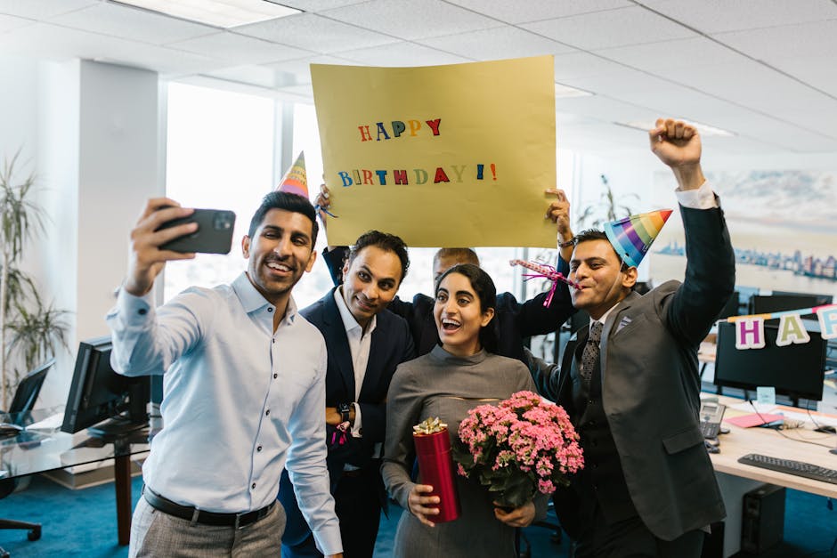 Group of colleagues celebrating a birthday in the office with gifts and a selfie.