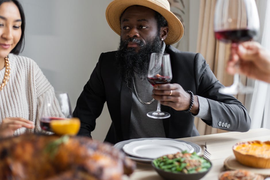 Positive diverse adult friends drinking wine while sitting at table served with delicious dishes and celebrating Thanksgiving Day