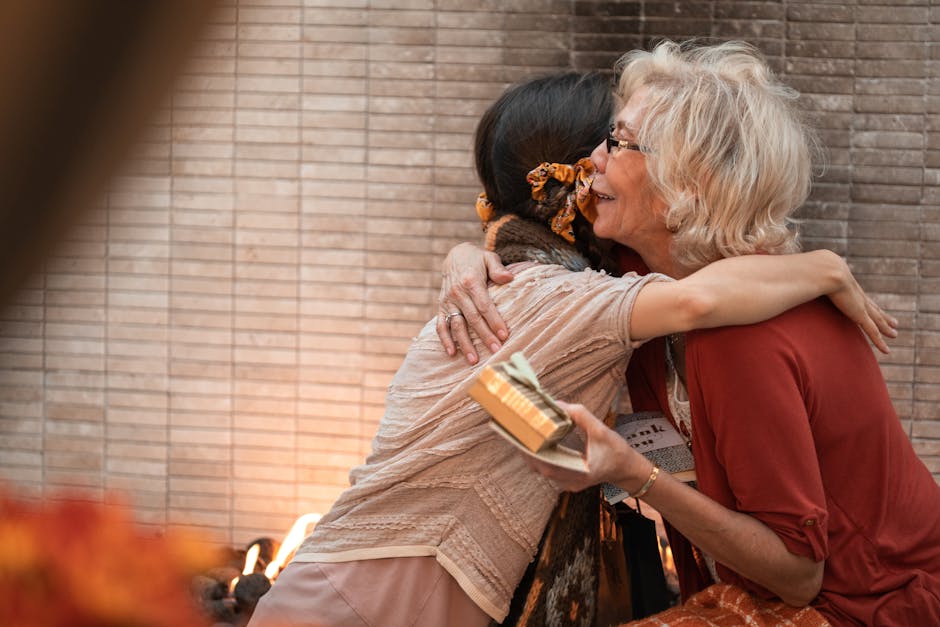 Elderly woman and younger woman sharing a heartfelt hug indoors, holding a gift.