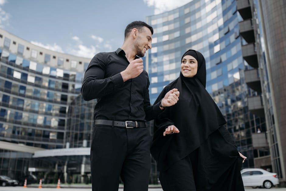 A smiling couple walking past a modern glass building in an urban environment.