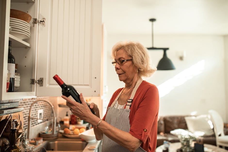 Elderly woman examining a wine bottle in a cozy kitchen setting.
